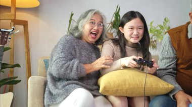 Torunlarıyla rahat bir oturma odasında video oyunu oynayan mutlu büyükanne ve büyükbaba.