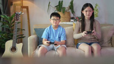 İki mutlu kardeş evlerinin rahat oturma odasında video oyunu oynuyorlar.