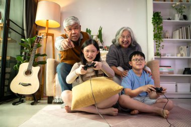 Torunlarıyla rahat bir oturma odasında video oyunu oynayan mutlu büyükanne ve büyükbaba.