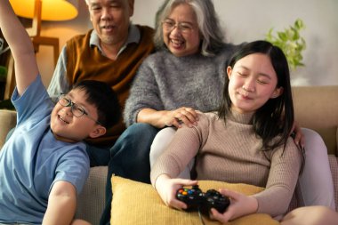 Torunlarıyla rahat bir oturma odasında video oyunu oynayan mutlu büyükanne ve büyükbaba.