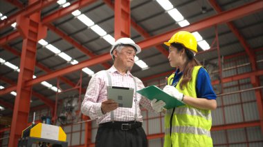 Kıdemli mühendisler ve genç bayan işçiler güvenlik miğferleri ve diğer ekipmanlarla üretim hattındaki makineleri konuşuyor ve denetliyorlar.