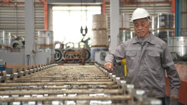 Kıdemli teknisyen, endüstriyel bir fabrikadaki üretim hattında büyük makineleri kontrol ediyor.