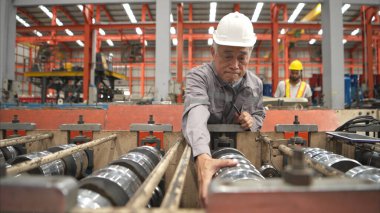 Kıdemli teknisyen, endüstriyel bir fabrikadaki üretim hattında büyük makineleri kontrol ediyor.