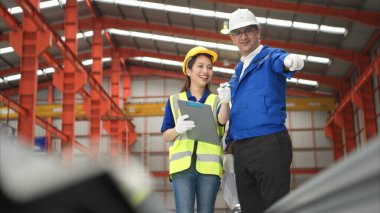 Kıdemli mühendisler ve genç bayan işçiler fabrikadaki üretim hattına gönderilmeden önce çok amaçlı oluşumlar için çelik levhaları konuşuyor ve inceliyorlar.