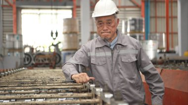Kıdemli teknisyen, endüstriyel bir fabrikadaki üretim hattında büyük makineleri kontrol ediyor.