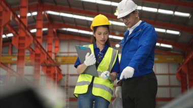 Kıdemli mühendisler ve genç bayan işçiler fabrikadaki üretim hattına gönderilmeden önce çok amaçlı oluşumlar için çelik levhaları konuşuyor ve inceliyorlar.
