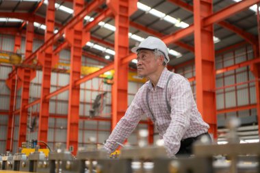 Kıdemli teknisyen, endüstriyel bir fabrikadaki üretim hattında büyük makineleri kontrol ediyor.