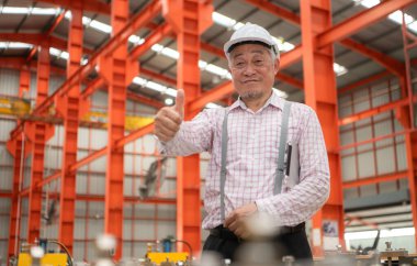 Kıdemli teknisyen, endüstriyel bir fabrikadaki üretim hattında büyük makineleri kontrol ediyor.