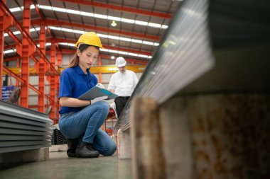 Kıdemli mühendisler ve genç bayan işçiler fabrikadaki üretim hattına gönderilmeden önce çok amaçlı oluşumlar için çelik levhaları konuşuyor ve inceliyorlar.