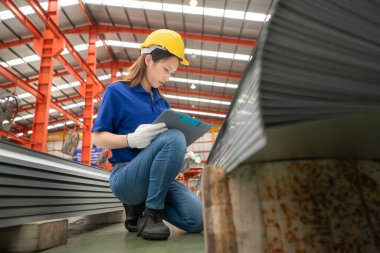 Genç bayan işçiler fabrikadaki üretim hattına gönderilmeden önce çok amaçlı oluşumlar için çelik levhaları konuşuyor ve inceliyorlar.