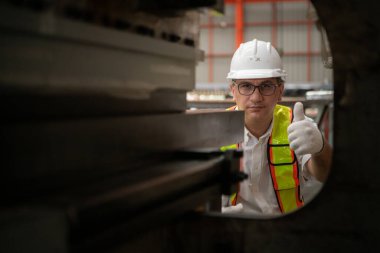 Kıdemli teknisyen, endüstriyel bir fabrikadaki üretim hattında büyük makineleri kontrol ediyor.
