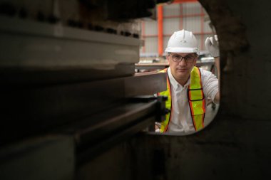 Kıdemli teknisyen, endüstriyel bir fabrikadaki üretim hattında büyük makineleri kontrol ediyor.