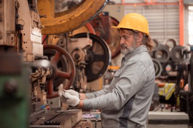 Kıdemli teknisyen metal levha fabrikasında büyük bir makineyi kontrol ediyor.