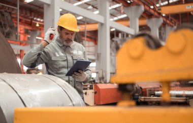 Kıdemli teknisyen, endüstriyel bir fabrikadaki üretim hattında büyük makineleri kontrol ediyor.