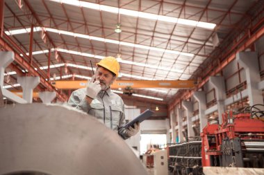 Kıdemli teknisyen, endüstriyel bir fabrikadaki üretim hattında büyük makineleri kontrol ediyor.