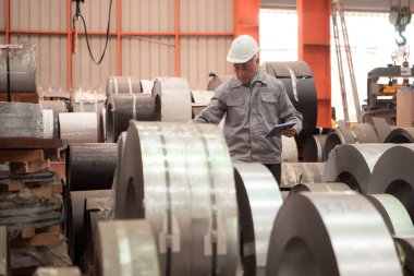 Endüstriyel kıdemli işçi güvenlik kaskı takan bir fabrikada büyük bir metal tüpü inceliyor.