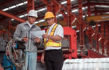 Bir grup endüstriyel işçi güvenlik kaskı takan bir fabrikada büyük bir metal tüpü inceliyor.