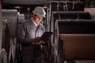 Sanayi işçisi, güvenlik kaskı takan bir fabrikada büyük bir metal tüpün içini inceliyor.