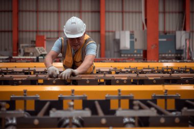 Kıdemli teknisyen, endüstriyel bir fabrikadaki üretim hattında büyük makineleri kontrol ediyor.