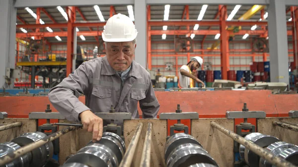 Kıdemli teknisyen, endüstriyel bir fabrikadaki üretim hattında büyük makineleri kontrol ediyor.