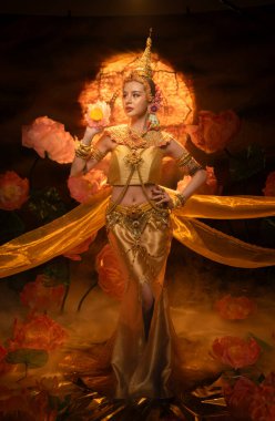 Geleneksel Tayland kostümü giymiş güzel bir kadın, altın ipek kumaş ve nilüfer çiçeğiyle klasik bir dans sergiliyor.