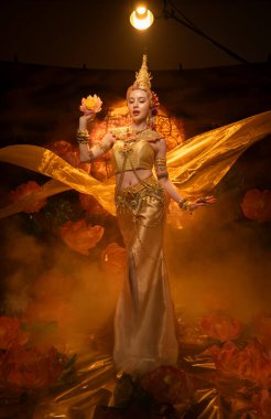 Geleneksel Tayland kostümü giymiş güzel bir kadın, altın ipek kumaş ve nilüfer çiçeğiyle klasik bir dans sergiliyor.