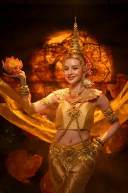 Geleneksel Tayland kostümü giymiş güzel bir kadın, altın ipek kumaş ve nilüfer çiçeğiyle klasik bir dans sergiliyor.