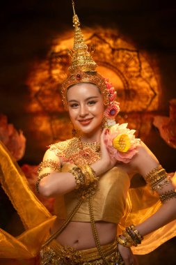Geleneksel Tayland kostümü giymiş güzel bir kadın, altın ipek kumaş ve nilüfer çiçeğiyle klasik bir dans sergiliyor.