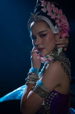 Geleneksel Güneydoğu Asya kostümü içinde zarif bir kadın. Nilüfer çiçekleri arasında dans ediyor. Yumuşak sahne ışıkları altında mavi kumaş akıyor.