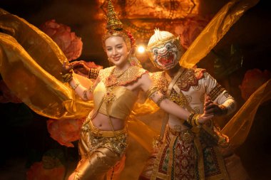 Geleneksel Tayland dansı gösterisinde zarif bir bayan dansçı ve altın kostümlü maskeli bir Khon sanatçısı, zarafet ve kültür mirasını sembolize ediyor.