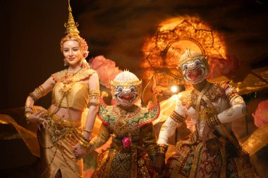 Geleneksel Tayland dansı gösterisinde zarif bir bayan dansçı ve altın kostümlü maskeli bir Khon sanatçısı, zarafet ve kültür mirasını sembolize ediyor.