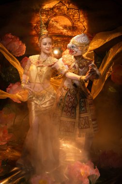 Geleneksel Tayland dansı gösterisinde zarif bir bayan dansçı ve altın kostümlü maskeli bir Khon sanatçısı, zarafet ve kültür mirasını sembolize ediyor.