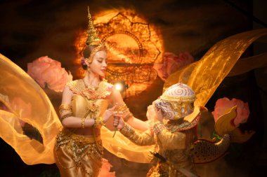 Geleneksel Tayland dansı gösterisinde zarif bir bayan dansçı ve altın kostümlü maskeli bir Khon sanatçısı, zarafet ve kültür mirasını sembolize ediyor.