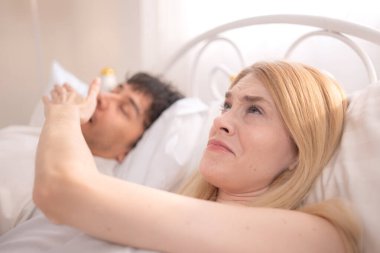 Ortağı yanında yüksek sesle horlarken elleri ile kocasının ağzını kapatan genç bir kadın.