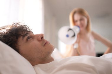 Sabahları ortağını uyandırmak için megafon kullanan oyuncu kadın, yatakta kulaklarını kapatıyor.