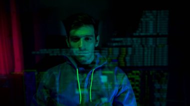 Maske takan ve kapüşonlu bir bilgisayar korsanı karanlık bir odada dijital verilerle etkileşime geçerek siber suç ve online güvenlik tehditlerini temsil ediyor.