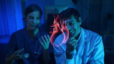 Doktorlar ve tıp uzmanları kalp sağlığını modern hastane ortamında fütürist hologram teknolojisiyle tartışıyor.