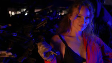 Kırmızı tulumlu seksi model bir tamirci dramatik ışıklandırma altında oto yedek parça deposunda güven içinde poz veriyor.