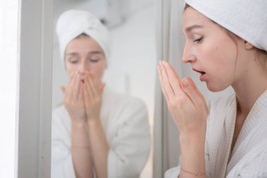 Genç bir kadın aynanın önünde duruyor, dişlerini fırçalıyor ve sabah diş sağlığını kontrol ediyor.