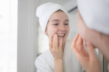 Genç bir kadın aynanın önünde duruyor, dişlerini fırçalıyor ve sabah diş sağlığını kontrol ediyor.