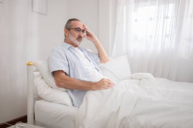 Yaşlı bir adam yatak odasına uzanmadan önce yatağında dinlenerek rahatlar.