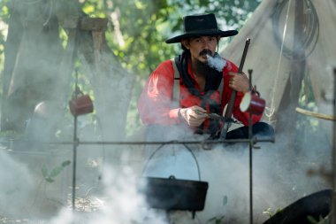 Kamp ateşinde yemek hazırlayan kovboylar, sıcak ve kırsal alanda birlikte et kızartıyorlar.
