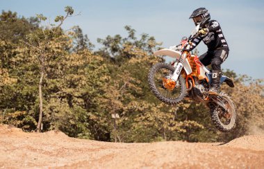 Bir motokros binicisi toprak bir pistte atlıyor, hız, güç ve off-road atletizm yeteneğini sergiliyor.