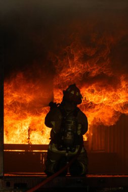 Yoğun ateş ve dumanla çevrili büyük bir yangını söndürmek için koruyucu giysili bir itfaiyeci çalışıyor.
