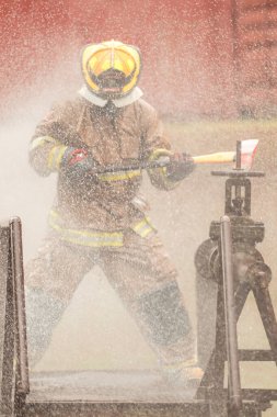 Koruyucu giysili bir itfaiyeci yangın musluğuna acil durum müdahalesi yaparken baltasını sallıyor. İtfaiyeci tehlikeli koşullar altında çalışırken su havaya sıçrıyor.