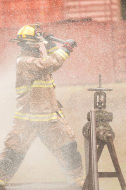 Koruyucu giysili bir itfaiyeci yangın musluğuna acil durum müdahalesi yaparken baltasını sallıyor. İtfaiyeci tehlikeli koşullar altında çalışırken su havaya sıçrıyor.