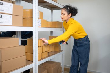 Kadın depo personeli karton kutuda barkodu tarıyor, depolama alanındaki envanter ve sipariş işlemlerini yönetiyor.