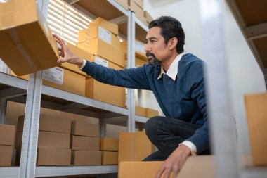 Depo çalışanı, depolama raflarındaki kutuları düzenlerken paket etiketlerini ve envanter detaylarını kontrol ediyor