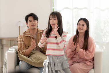 Genç bir kız anne ve babası için oturma odasında dans eder. Onlar gülümseyip alkışlarken, sıcak ve neşeli bir aile anını yakalar.