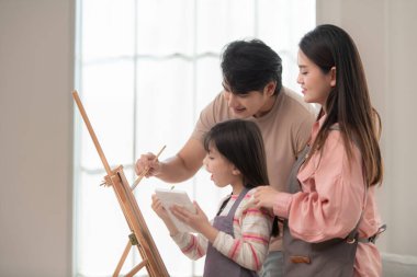 Ebeveynler kızlarına sehpada resim yaparken rehberlik ederler. Birlikte yaratıcı bir aile aktivitesinin tadını çıkarırlar.